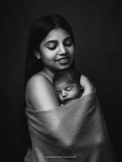 A tender black and white portrait of a mother holding her sleeping newborn. The soft wrap and her gentle smile create a feeling of pure serenity.