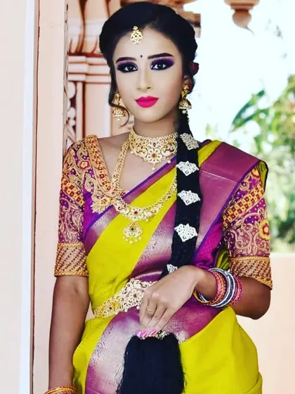 This model is styled in a vibrant yellow and purple saree. The makeup is bold to match, with dramatic purple winged eyeshadow and a bright fuchsia lip for a contemporary twist on a traditional look.