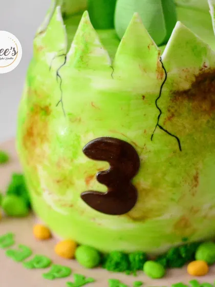 A dinosaur is hatching. This dino egg cake is perfect for a young dinosaur enthusiast's third birthday.