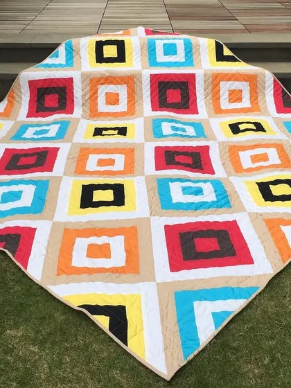 A bright and bold quilt with a "square in a square" pattern, laid out on the grass.