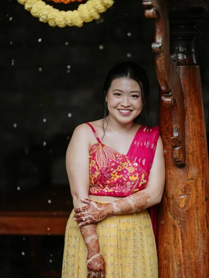 A lovely portrait of the bride in her vibrant Haldi outfit, standing by a traditional wooden pillar before the ceremony begins.