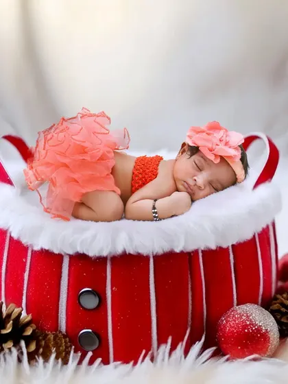 A festive Christmas-themed photo with a newborn sleeping in a Santa-style basket.