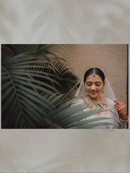 A serene portrait of the bride framed by a palm leaf, adding a natural and soft element to the shot.