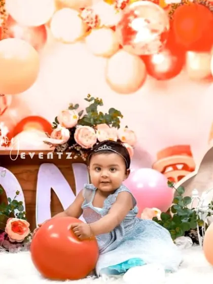 A festive and fun cake smash photoshoot in our Bangalore studio. This setup is filled with peach and white balloons, floral arrangements, and a "ONE" sign, perfectly capturing the celebratory spirit of a first birthday.