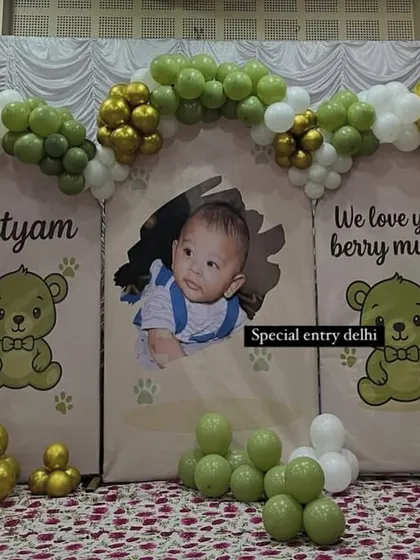 A cute teddy bear themed birthday backdrop for Nityam. The setup includes custom printed panels and a green, white, and gold balloon arch.
