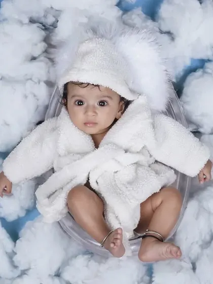 An overhead shot of a baby in a white bathrobe and hat, nestled among soft cotton clouds. I prioritize your baby's comfort and safety while creating these imaginative scenes.
