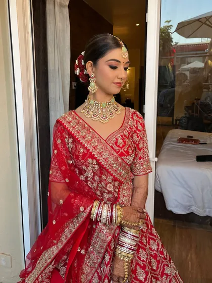 A classic bridal pose for Hershee. Her makeup features a flawless base and defined eyes, paired with an elegant hair bun adorned with red roses for a traditional touch.