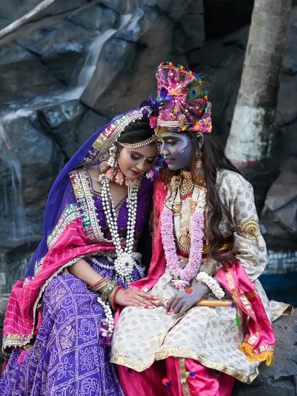 A serene photo of Radha and Krishna by a waterfall.