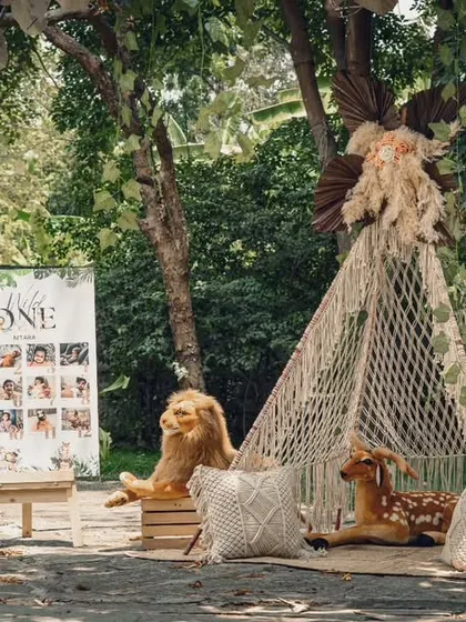 The complete "Wild ONE" setup in an outdoor setting. The macrame teepee, milestone photo board, and plush animals create a beautiful and engaging space for a first birthday.