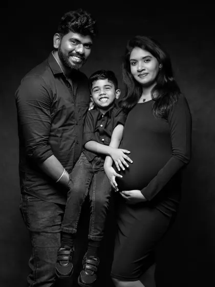 A timeless black and white family portrait. This classic studio shot focuses on the family's connection and joy, with the simple dark clothing and background ensuring that their expressions are the main story.