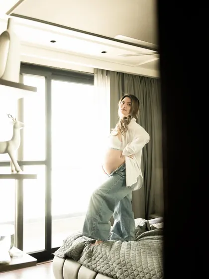 A confident and modern pose on the bed. The combination of a simple white shirt and jeans creates a look that is both stylish and relaxed.
