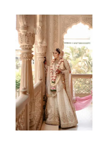 The bride, holding her varmala, waits in a beautifully carved temple corridor. The setting adds a sense of divinity to the moment.