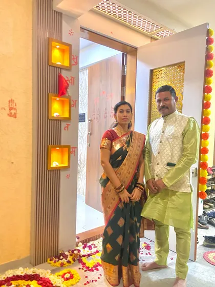 The proud homeowners, Mr. and Mrs. Suryavanshi, at the entrance of their newly designed home, decorated for the housewarming ceremony.