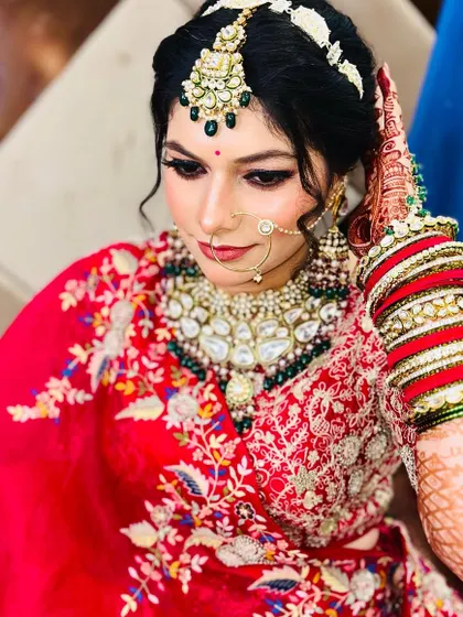 A beautiful bride in a traditional red and gold outfit. Her makeup is classic and elegant, with a focus on her eyes and flawless skin.