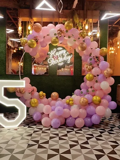 A pretty pink and purple balloon arrangement for a 5th birthday party in a restaurant. The setup includes a half-moon balloon arch and a large light-up number "5".