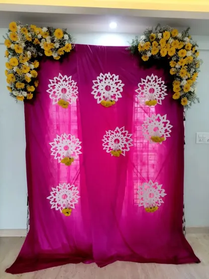 A simple floral backdrop with a pink drape, suitable for a small puja or home function.
