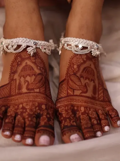 The rich, dark stain on these bridal feet is just stunning. The design features peacocks under a royal umbrella, paired with beautiful silver anklets.