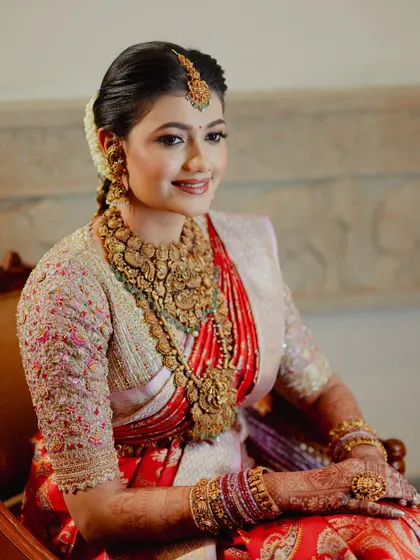 A portrait of a radiant South Indian bride, her hands adorned with a rich mehendi stain that complements her red silk saree.