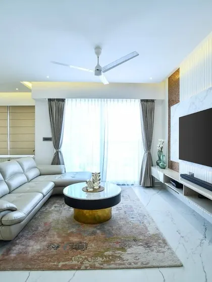 A modern living room where the TV wall combines a marble-finish panel with fluted details and warm backlighting. The space is designed to feel clean and airy, with a large sectional sofa providing ample comfort.