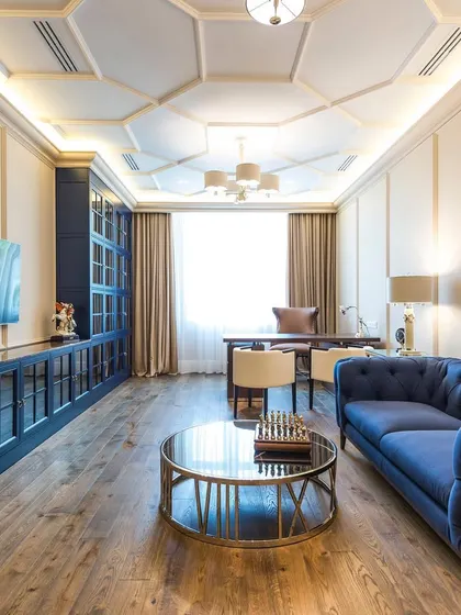 A different angle of the modern-classic living room, highlighting the seamless integration of the TV unit within the custom blue cabinetry and the elegant wooden flooring.