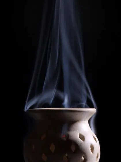Wisps of smoke rise gracefully from a ceramic pot against a solid black background. This minimalist and abstract photograph focuses on form and movement.