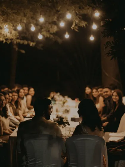 A view from behind the couple as they sit at their engagement dinner, surrounded by friends and family.