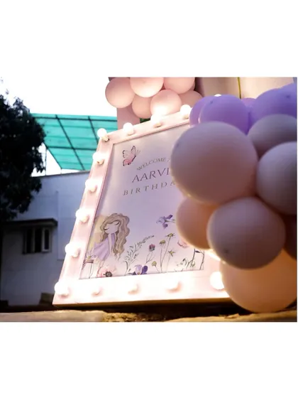 A close-up of the illuminated welcome sign for 'Aarvi's Birthday', surrounded by pastel balloons, setting a magical tone for a fairy-themed celebration.