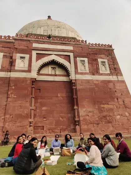 A moment of rest and reflection for the group in front of Ghiyasuddin Tughluq's tomb. This fortified mausoleum, built of red sandstone and white marble, is a starkly beautiful example of early Sultanate architecture.