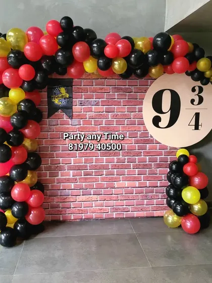 A Harry Potter theme decoration featuring a Platform 9 3/4 backdrop against a brick wall, with balloons in house colors.