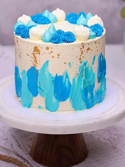 We create a piece of modern art with this abstract blue buttercream cake. Strokes of various blue shades are painted onto a white canvas, accented with gold splatters and topped with piped rosettes, making it a stylish and happy choice for a Father's Day celebration.