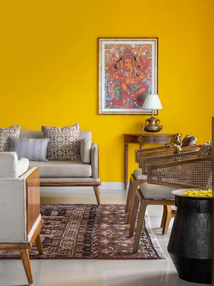 The quintessential ethnic setting of the 'Vasudhalayah' living room is elevated by a bold yellow accent wall, a Ganesha painting, and curated furniture, creating a vibrant and culturally rich atmosphere.