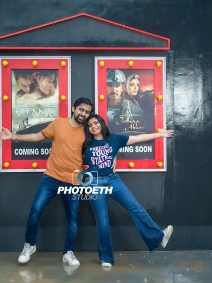 A fun, movie-themed pre-wedding shot. The couple poses playfully in front of mock movie posters, creating a unique and personalized photograph.