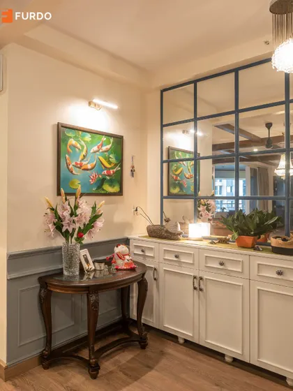 A detailed view of the grand foyer in the Brigade Exotica home, showcasing the blend of artwork, mirrors, and classic furniture.
