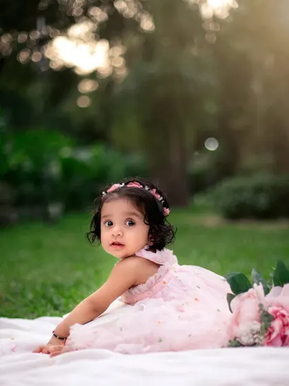 A dreamy outdoor portrait. The soft, golden light and lush green background create a magical atmosphere for this little girl's first birthday photos.