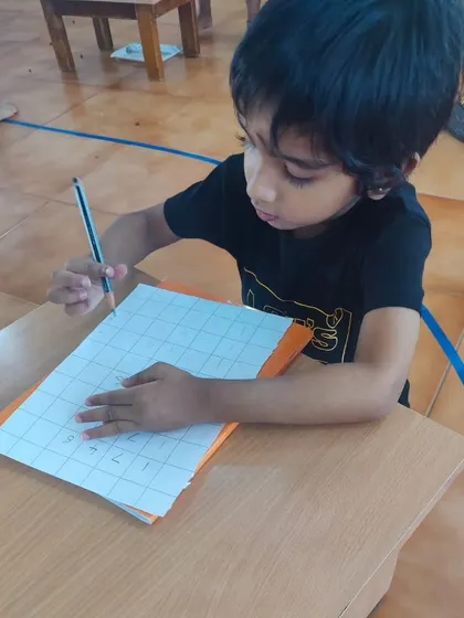 A child practices writing numbers on a gridded sheet. This activity helps with number formation, spacing, and developing the fine motor control needed for neat handwriting.