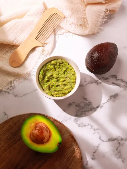 A bright and fresh shot of a DIY avocado hair mask. The use of a marble background, natural light, and a halved avocado makes the image look clean, healthy, and appealing.