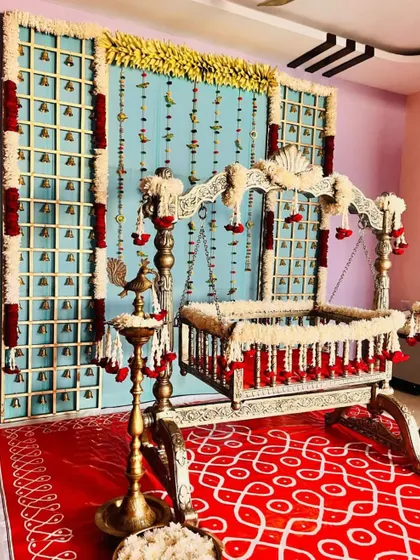 A divine naming ceremony setup with a silver cradle. The backdrop features panels with bells and hanging flower strings, creating a beautiful sound and sight experience.