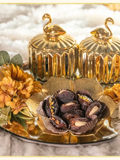 This stunning gold-themed hamper is perfect for Eid celebrations. It features ornate swan-topped jars and a floral bowl filled with almond-stuffed dates, all on a mirrored tray.