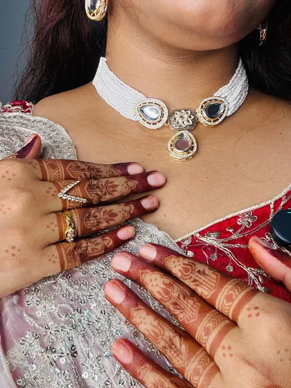 A close-up of the beautiful henna stain on the fingers, adorned with elegant rings and a statement necklace.