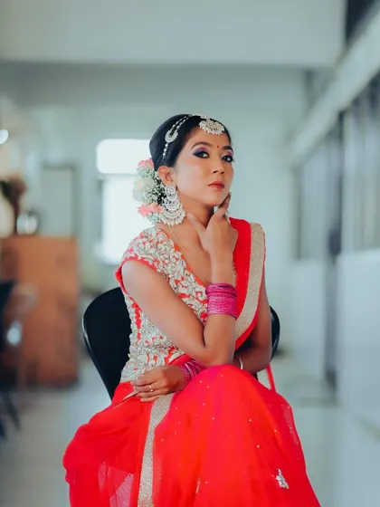 A seated portrait in an indoor setting. The bride's pose is confident and poised, showcasing her stunning red and silver outfit.