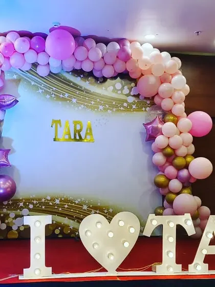 A personalized naming ceremony stage for Tara. The backdrop features a beautiful balloon arch in pastel pinks and gold, with large light-up marquee letters that make a wonderful centerpiece.