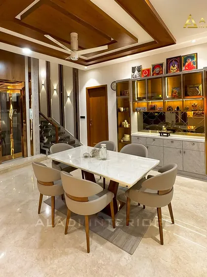 This dining space exudes luxury with a marble-top table, plush upholstered chairs, and a stunning glass crockery unit with internal lighting. The wooden ceiling panels and intricate wall details add layers of warmth and sophistication.