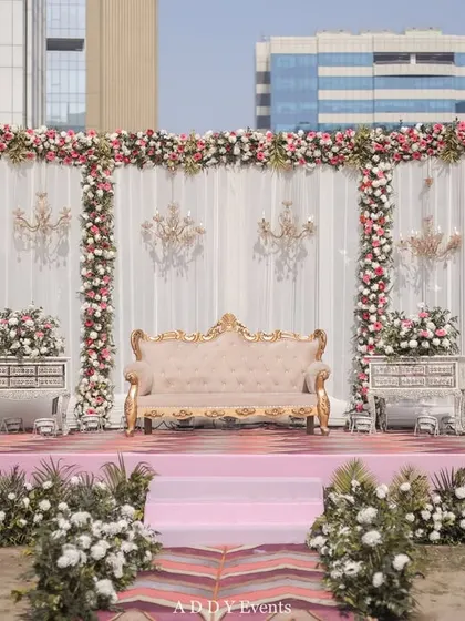 We created this royal-themed outdoor stage with a backdrop of white drapes, floral borders, and hanging crystal chandeliers. The blush pink stage and vintage-style sofa add a touch of softness and romance to the grand design.