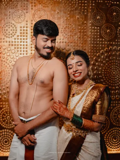 A happy portrait of the couple in their traditional South Indian attire against a stunning gold-textured wall.