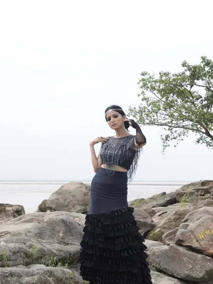Part of a conceptual outdoor shoot, this look features a black ruffled skirt and embellished top set against a rocky, natural landscape. The styling was intended to create a dramatic, almost elemental fashion story.