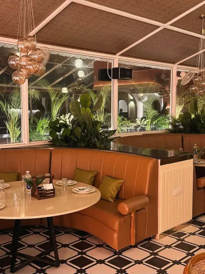 Curved, tan leather banquettes create a comfortable and social seating arrangement at Tipsy Town. The design incorporates lush greenery behind the seating, blurring the line between indoors and outdoors and enhancing the biophilic feel of the restaurant.