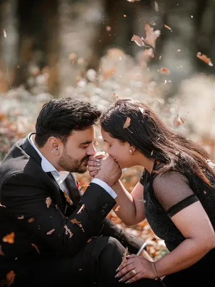 An intimate pre-wedding portrait in a forest setting, with autumn leaves falling around the couple. The warm colors and romantic action create a fairytale-like image.