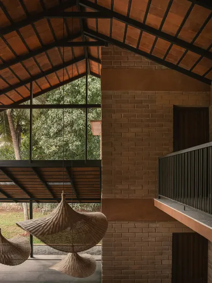 A view from the upper floor shows the double-height volume of the living space. The large window frames the lush greenery outside, making it a living piece of art, while the balcony provides a connection between levels.