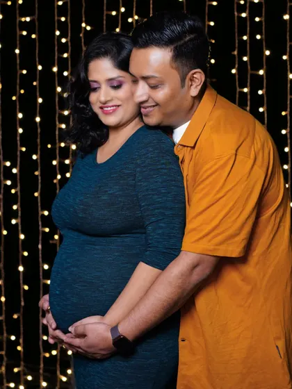A loving embrace from behind, with the couple smiling against a warm, sparkling background. This studio setup with fairy lights adds a touch of magic to the maternity shoot.