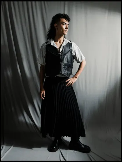 A full-length shot of a model in a gender-fluid outfit. The dramatic lighting and shadows create a powerful, high-contrast image.